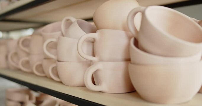 A pile of handmade ceramic dishes lying on a rack in a pottery workshop. View of various handmade pottery at pottery studio.