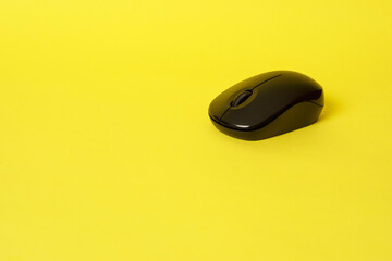 A black wireless computer mouse on a bright yellow background.