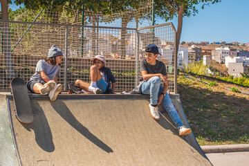 Three child skaters, with their skates, sitting on an obstacle on the skate park, talking and...