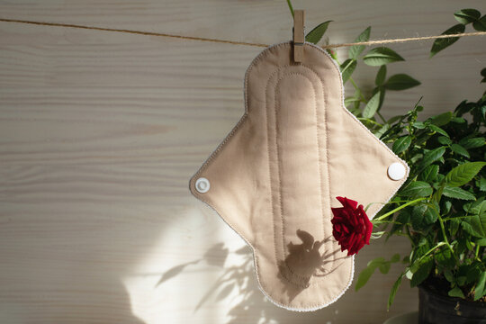 Eco-friendly reusable organic bio-cotton pad hanging on a rope on a wooden background with a rose bush, hard shadows on in the light. Zero waste reusable washable cloth pad.