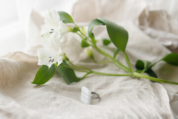 Fototapeta na wymiar Stylish modern white square ring and alstroemeria beautiful flower on linen textile, copy space. Unusual fashionable fused glass ring. Contemporary gift