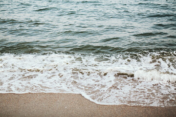 Sea waves and foam on sandy beach close up in evening time. Tranquil and calm moment. Summer vacation and travel concept. Mindfulness