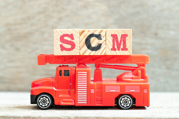 Fire ladder truck hold letter block in word SCM (Abbreviation of Supply chain management) on wood background