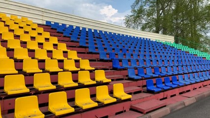 Yellow, green, red and blue seats in a row in the stadium without the player and the audience. Empty stadium or race track seats during the COVID-19 coronavirus pandemic. - Powered by Adobe