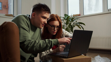 A man and his girlfriend use a laptop to buy furniture in an apartment