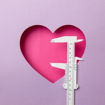 Pink heart on a purple background. At the heart is a white micro meter. Concept measuring love. Copy space
