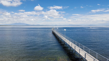 Long wooden fishing pier to the lake in San Rafael, Mendoza. Calm blue waters and a clouds in the sky with a background of the mountains on a summer day.