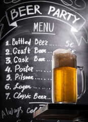 Draft beer in a mug with foam on a bar counter at the chalk board background with menu in a pub.
