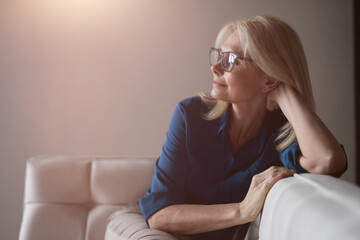Calm mature woman in eyewear relaxing on a couch at home in the living room