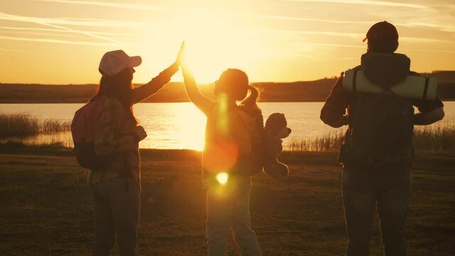 Happy family concept. Teamwork family hiking in nature. Daughter and parents with backpacks at sunset. Silhouette of a family playing pilots while hiking. Friendly family summer vacation together.
