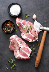 Fresh meat. Raw pork steak with spices, ax and garlic on a black background. View from above.
