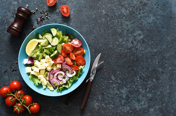 Mix salad with vegetables, leaves and feta. Greek salad in a plate on a blue concrete background. View from above.