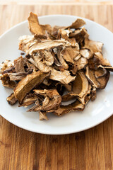 Dry dehydrated sliced mushrooms on a white dish wooden background close up shot