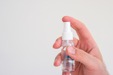 Small plastic hand sanitizer bottle with spray head held in hand by Caucasian male hand isolated close up shot