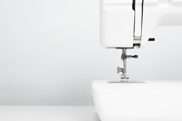 Electric white sewing machine. Close-up of a needle and thread. Professional sewing equipment standing on a table on a light background, copy space.