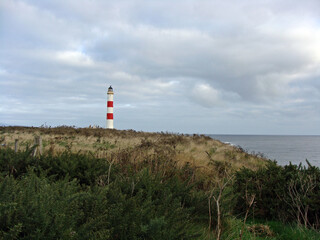 Fototapeta na wymiar Leuchtturm rot weiß auf einer Wiese vor dem Meer, an der Küste, bewölkt, draußen, Tag