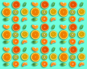 Pattern made with fresh Mandarins, sliced oranges, kiwi and mint leaves on green surface. Flat lay
