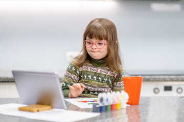 A girl with down syndrome is engaged in lessons using a tablet. Down child is engaged in drawing during an online lesson. Accessibility of education for children with disabilities
