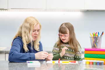 A girl with down syndrome sits next to her mother and is engaged in creativity, drawing a picture...