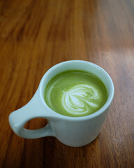 Cup of green tea latte on wooden table closeup.
