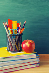 Back to school background. Pens, pencils, rulers, scissors in a glass, a red apple, a stack of...