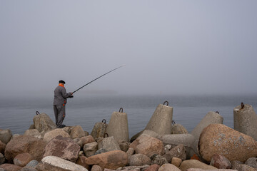 pier in the Baltic Sea where along the edges are concrete blocks, on which stands a fisherman with a rod