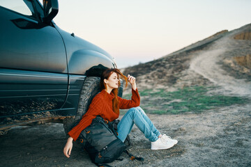 woman travels on nature in the mountains near the car with a backpack on the side