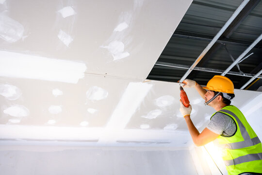 Young male construction workers wearing uniforms Installing gypsum ceiling inside the house and building. Using an electric screwdriver to drill to install the ceiling inside the house.