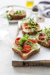 Healthy sandwich with cream cheese, baked tomatoes and micro greens on white background. Healthy breakfast sandwiches on a wooden board