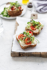Healthy sandwich with cream cheese, baked tomatoes and micro greens on white background. Healthy breakfast sandwiches on a wooden board