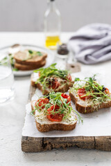 Healthy sandwich with cream cheese, baked tomatoes and micro greens on white background. Healthy breakfast sandwiches on a wooden board