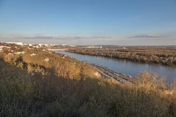 Nice view from the mountain to the river and the city. City on the river bank. Evening warm sunlight. Blue sky.