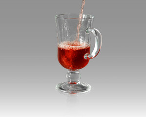 A glass into which a red drink (wine, juice) is poured on a gradient gray background.