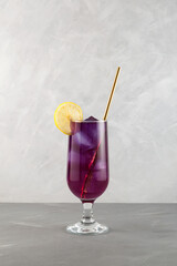 Purple cocktail served lemon and drinking straw. Summer refreshing drink. Grey background, copy space
