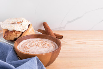 Cinnamon roll, cinnamon sticks, and cinnamon yogurt on wooden surface