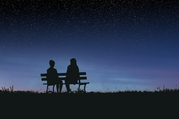 Silhouettes of two female friends sitting together and watching a spectacular night sky