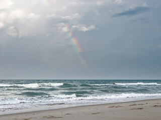 Calmful ocean beach dusk sunset with rainbow in deep blue sky and breezing waves.