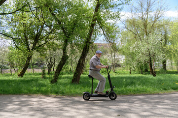 A positive, charismatic elderly man rides an eco scooter in the park. Walk in nature. Healthy lifestyle of the elderly. © mira_y