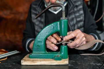 Closeup wrinkled hands of a senior man making holes in leather strap with puncher