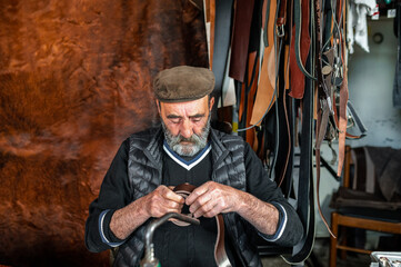 Portrait of senior bearded craftsman holding and making a genuine leather strap.