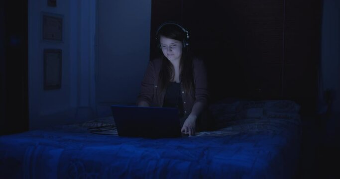A young woman listening to music on her laptop, while watching some videos at night. Slow motion.