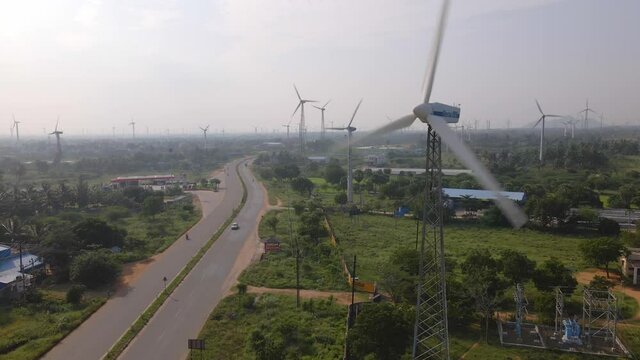A landscape drone aerial moving shot of a two-lane busy roadway dividing huge farm of wind turbines on a bright sunny day in India. sustainable, clean and renewable energy concept 