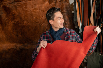 young male holding a piece of red genuine leather. Artisan feel and check the quality from the touch and softness of texture.