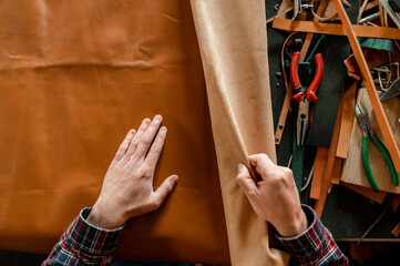 Top view unrecognizable male hands working with genuine leather in his workshop.