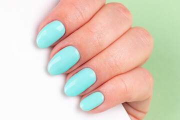 Female hand with beautiful manicure - mint blue nails with white smartphone on green background, closeup. Selective focus