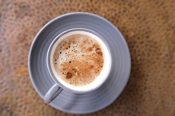 Cappuccino coffee in gray cup and saucer on an old copper table, ruddy fresh croissants, concept fresh pastries, morning coffee, caffeine addiction, energy boost