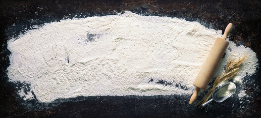 Abstract baking background with the rolling pin and flour on dark table