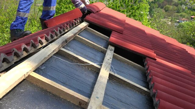 Construction worker on a roof covering it with tiles - roof renovation, roofing