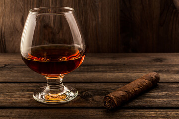 Glass of brandy and cuban cigar on a wooden table. Focus on the cuban cigar