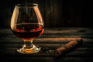 Glass of brandy and cuban cigar on a wooden table. Focus on the cuban cigar